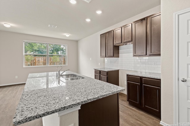 kitchen with a kitchen island with sink, light hardwood / wood-style flooring, and light stone countertops