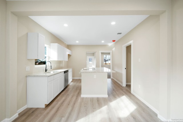 kitchen with dishwasher, white cabinets, sink, light hardwood / wood-style floors, and a kitchen island