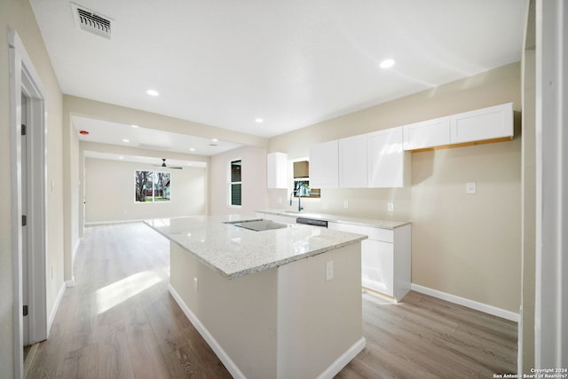 kitchen with light stone counters, a center island, white cabinets, and light hardwood / wood-style floors