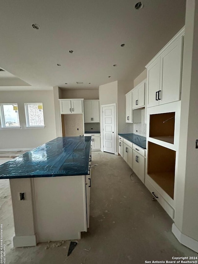 kitchen featuring concrete flooring, white cabinetry, a kitchen island, and dark stone counters