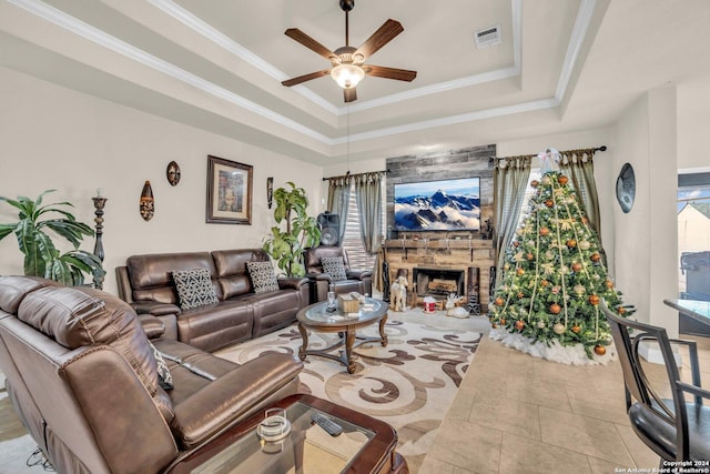 living room featuring a raised ceiling, crown molding, a fireplace, and ceiling fan