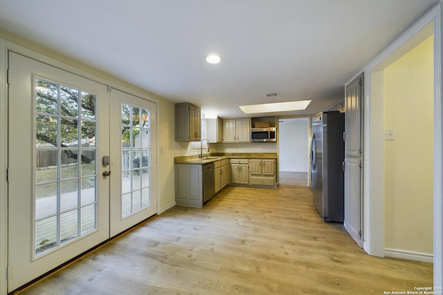 kitchen with a skylight, french doors, sink, stainless steel appliances, and light hardwood / wood-style flooring