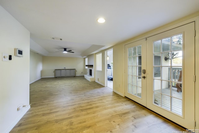 empty room with radiator, ceiling fan, french doors, a fireplace, and light wood-type flooring