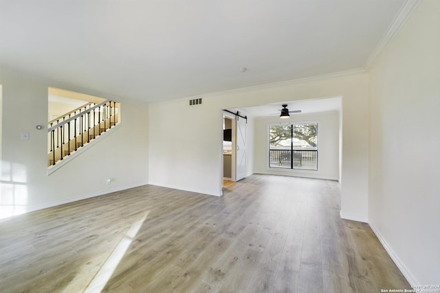 unfurnished living room with a barn door, light hardwood / wood-style floors, ceiling fan, and crown molding