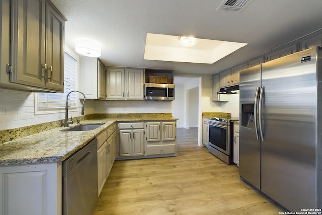 kitchen with sink, stainless steel appliances, light stone counters, light hardwood / wood-style flooring, and backsplash