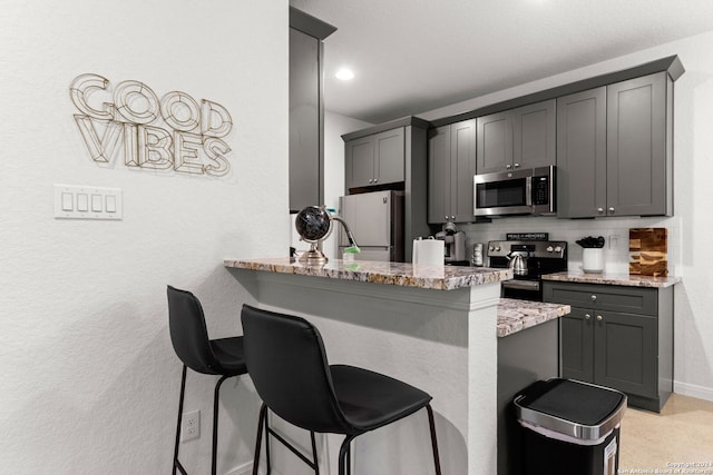 kitchen with tasteful backsplash, gray cabinets, light stone counters, and stainless steel appliances