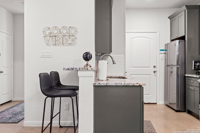 kitchen with light stone countertops, stainless steel refrigerator, gray cabinetry, and sink