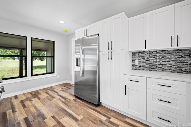 kitchen with white cabinets, decorative backsplash, stainless steel fridge, light stone countertops, and light hardwood / wood-style floors