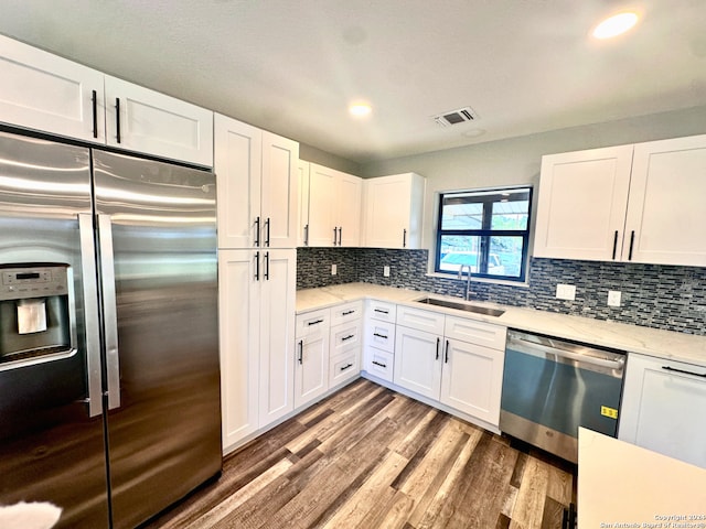 kitchen with appliances with stainless steel finishes, tasteful backsplash, sink, hardwood / wood-style flooring, and white cabinets