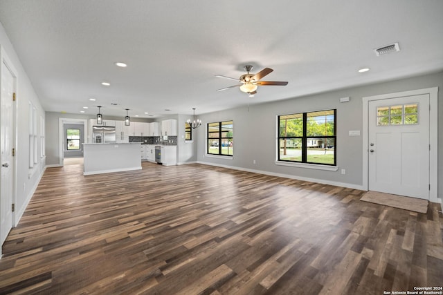 unfurnished living room with ceiling fan with notable chandelier and dark wood-type flooring