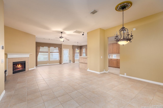 unfurnished living room featuring ceiling fan with notable chandelier, light tile patterned floors, and a tile fireplace