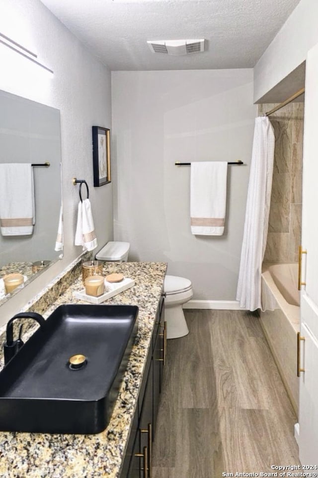 full bathroom with vanity, toilet, shower / bath combo with shower curtain, a textured ceiling, and wood-type flooring