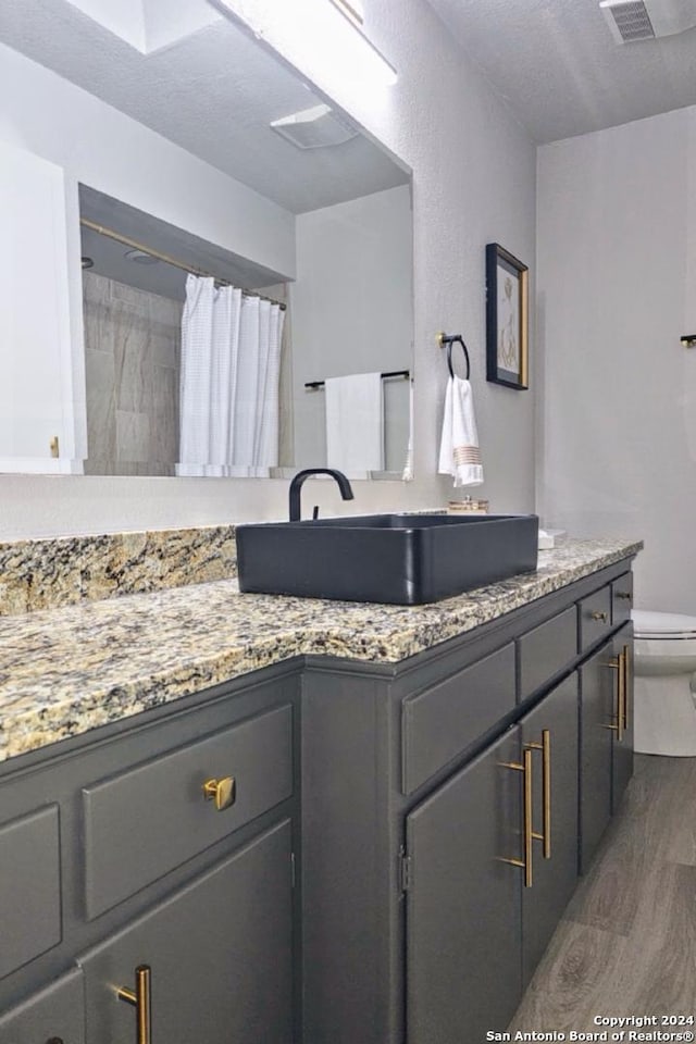 bathroom featuring vanity, hardwood / wood-style flooring, a shower with shower curtain, toilet, and a textured ceiling