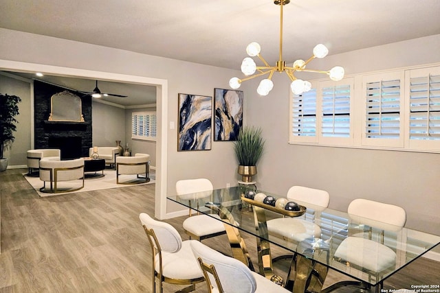 dining space featuring wood-type flooring, ceiling fan with notable chandelier, and a stone fireplace