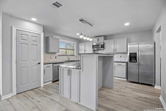 kitchen featuring hanging light fixtures, stainless steel appliances, backsplash, light hardwood / wood-style floors, and a kitchen island