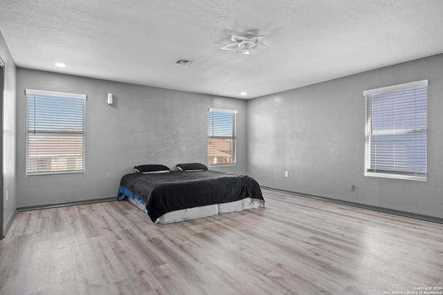 bedroom with light wood-type flooring, a textured ceiling, and multiple windows