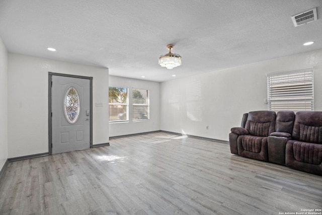 foyer entrance with a chandelier, a textured ceiling, and light wood-type flooring