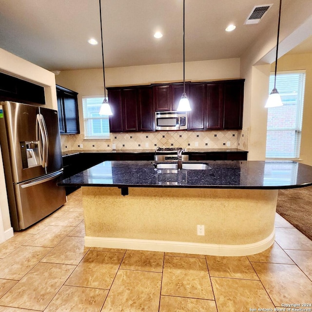 kitchen featuring dark stone counters, a center island with sink, stainless steel appliances, and sink