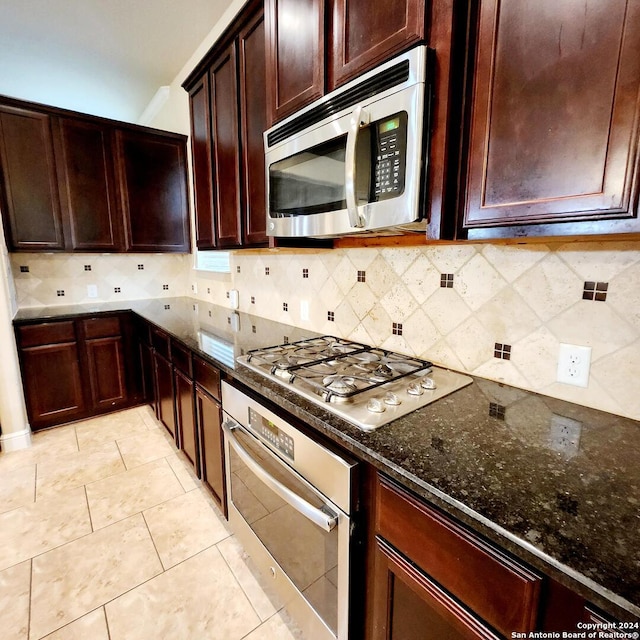 kitchen featuring appliances with stainless steel finishes, backsplash, light tile patterned floors, and dark stone countertops