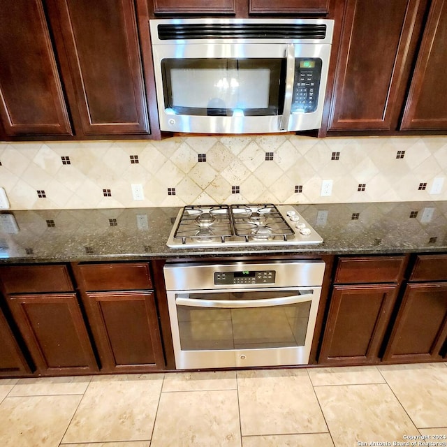 kitchen with backsplash, light tile patterned floors, stainless steel appliances, and dark stone counters