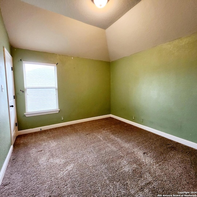 spare room featuring carpet flooring, a textured ceiling, and vaulted ceiling