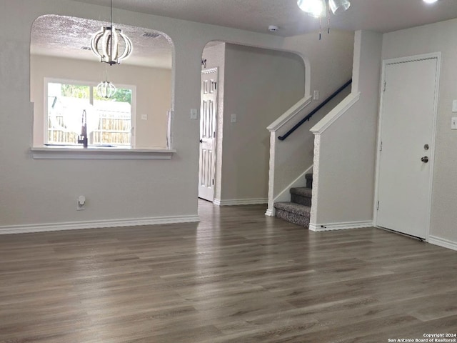 unfurnished living room featuring a notable chandelier, dark hardwood / wood-style floors, and a textured ceiling