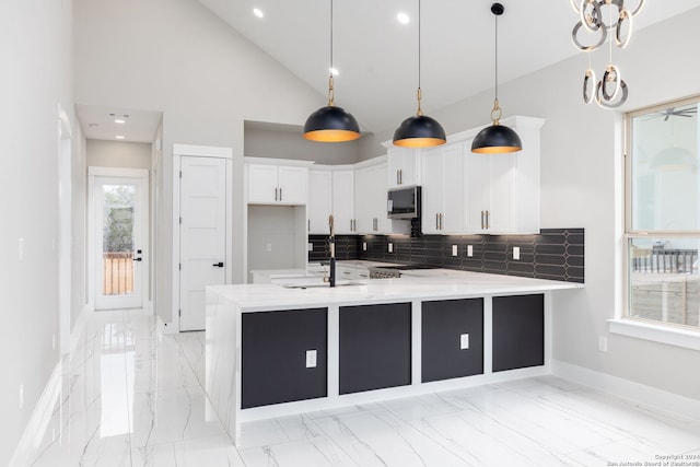 kitchen with backsplash, white cabinets, sink, hanging light fixtures, and light stone countertops