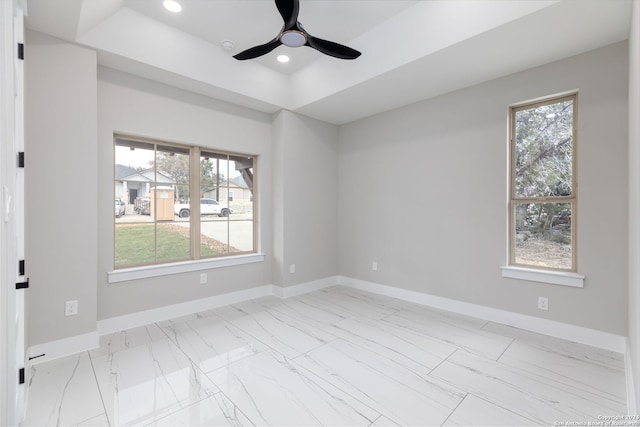 empty room with ceiling fan, a raised ceiling, and a wealth of natural light