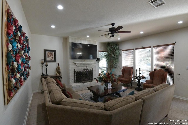 living room with ceiling fan, light tile patterned floors, a textured ceiling, and a brick fireplace