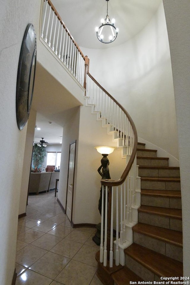 stairway featuring tile patterned floors, a towering ceiling, and ceiling fan with notable chandelier