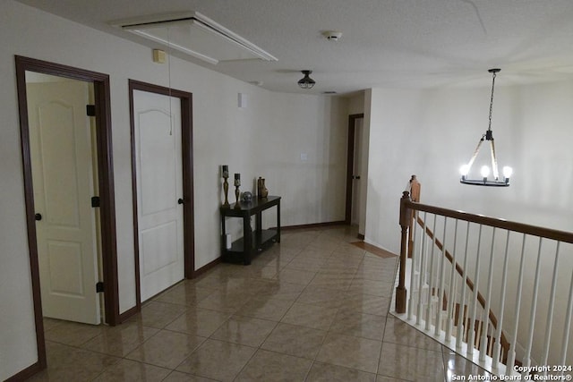 corridor featuring tile patterned floors, a textured ceiling, and an inviting chandelier