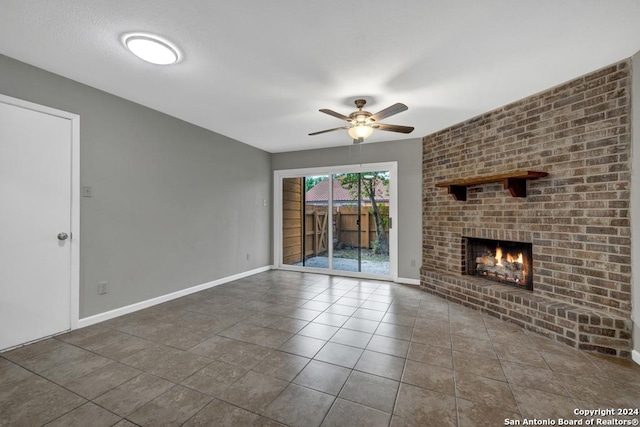 unfurnished living room featuring a fireplace, dark tile patterned flooring, and ceiling fan