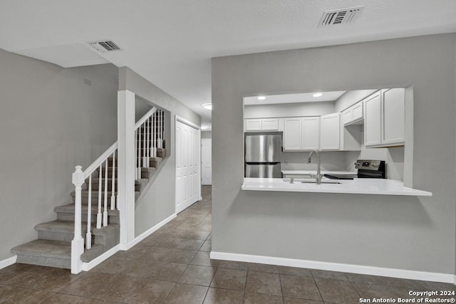 kitchen with white cabinets, dark tile patterned flooring, sink, kitchen peninsula, and stainless steel appliances