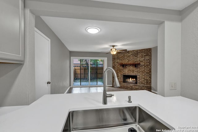 kitchen featuring kitchen peninsula, a brick fireplace, ceiling fan, sink, and white cabinetry