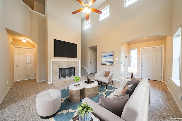 living room with a towering ceiling, light carpet, a wealth of natural light, and a tiled fireplace