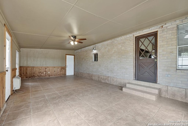 interior space with ceiling fan, wood walls, radiator, and brick wall