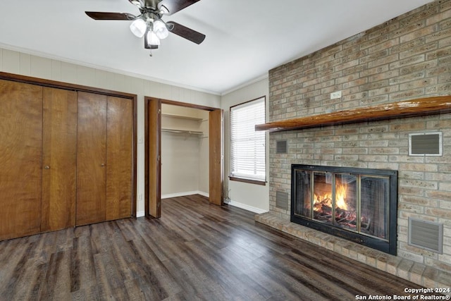 unfurnished living room featuring dark wood-type flooring, a brick fireplace, ceiling fan, and crown molding