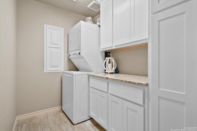 clothes washing area featuring stacked washer / drying machine and cabinets