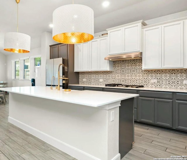 kitchen featuring decorative light fixtures, white fridge, white cabinetry, and a center island with sink