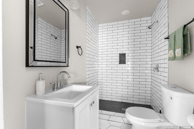 bathroom featuring tile patterned flooring, a tile shower, vanity, and toilet