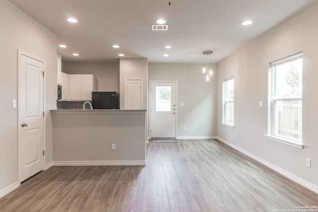 kitchen featuring kitchen peninsula, black refrigerator, white cabinetry, and a healthy amount of sunlight