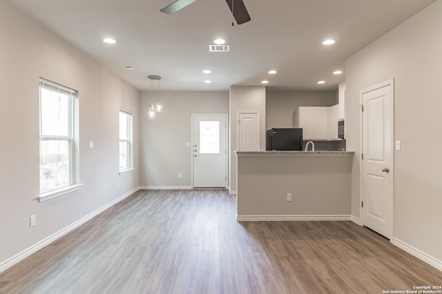 kitchen with kitchen peninsula, white cabinets, black appliances, ceiling fan with notable chandelier, and light wood-type flooring