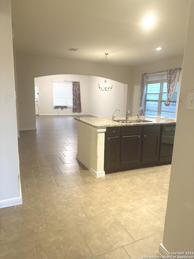 kitchen with light stone counters, dark brown cabinetry, sink, decorative light fixtures, and an inviting chandelier