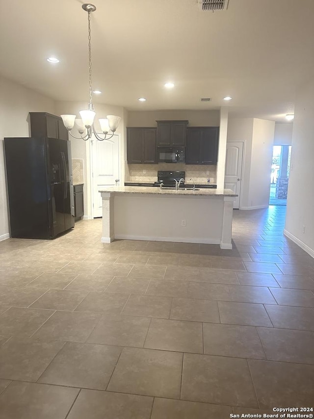 kitchen featuring tasteful backsplash, an island with sink, black appliances, and decorative light fixtures