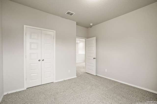 unfurnished bedroom featuring light carpet, a closet, and a textured ceiling