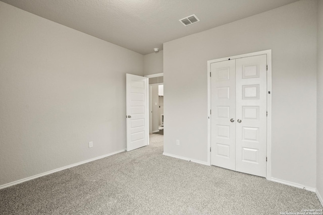 unfurnished bedroom with light colored carpet, a textured ceiling, and a closet