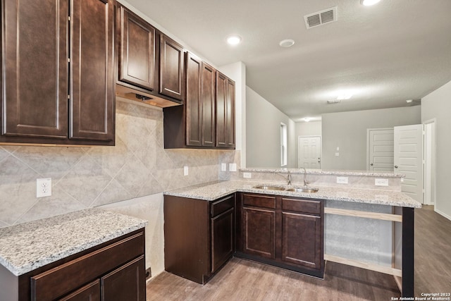 kitchen with sink, dark brown cabinetry, light stone countertops, light wood-type flooring, and kitchen peninsula