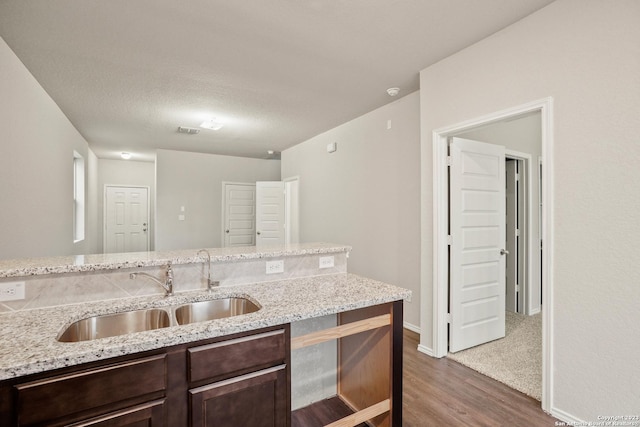 kitchen featuring hardwood / wood-style floors, dark brown cabinets, light stone counters, and sink