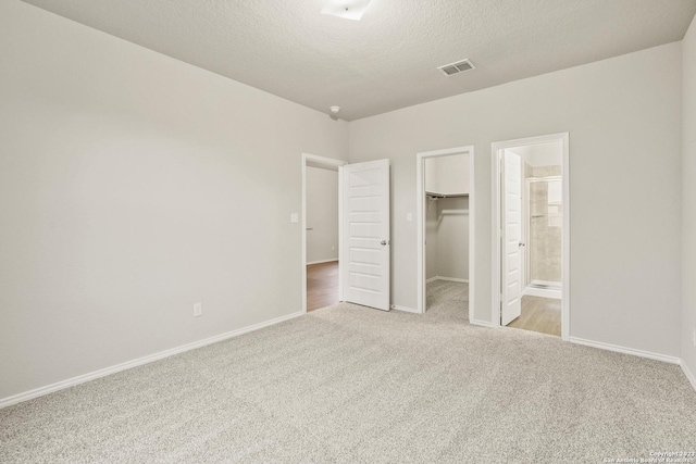 unfurnished bedroom with a walk in closet, ensuite bath, a textured ceiling, light colored carpet, and a closet