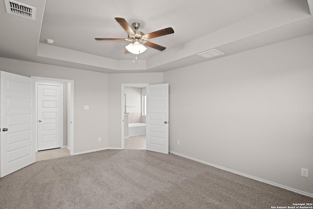 unfurnished bedroom featuring ensuite bath, ceiling fan, a tray ceiling, light carpet, and a closet